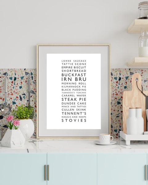 Minimalist framed wall print, displaying a vertical list of iconic Scottish foods and drinks in clean black typography on a white background. The design features items such as lorne sausage, tattie scone, Irn Bru, Buckfast, steak pie, Cullen skink, Tennent’s, and stovies. Styled in a neutral interior.
